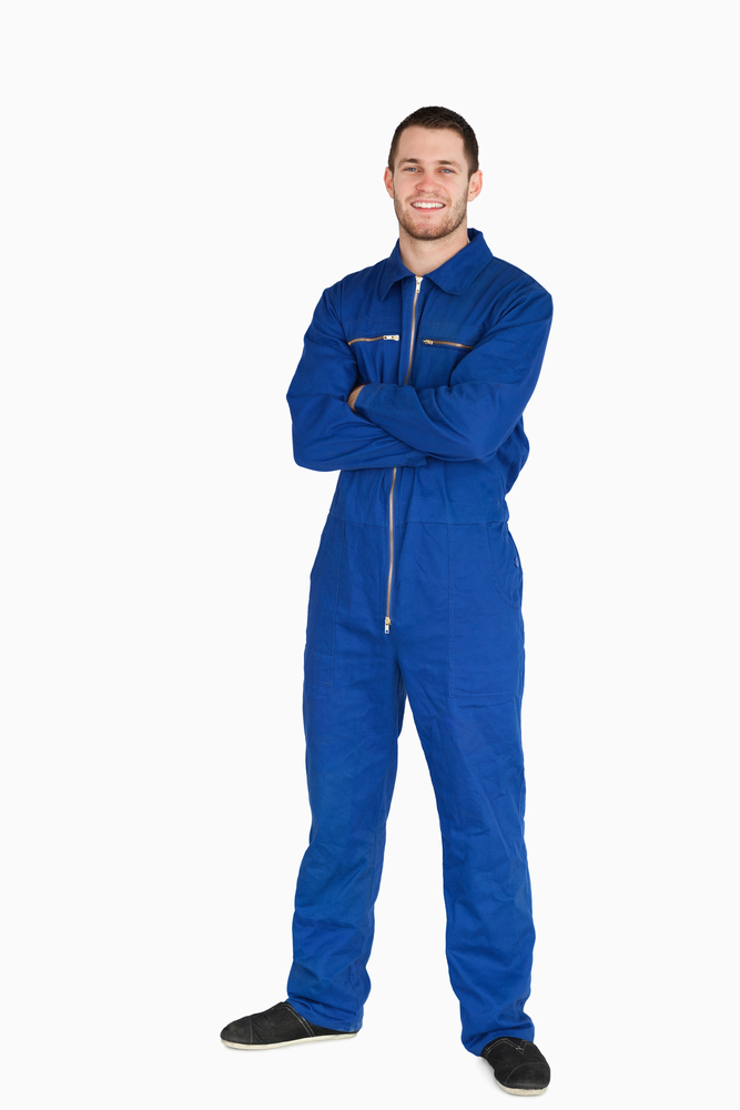 Smiling young mechanic in boiler suit with arms folded against a white background